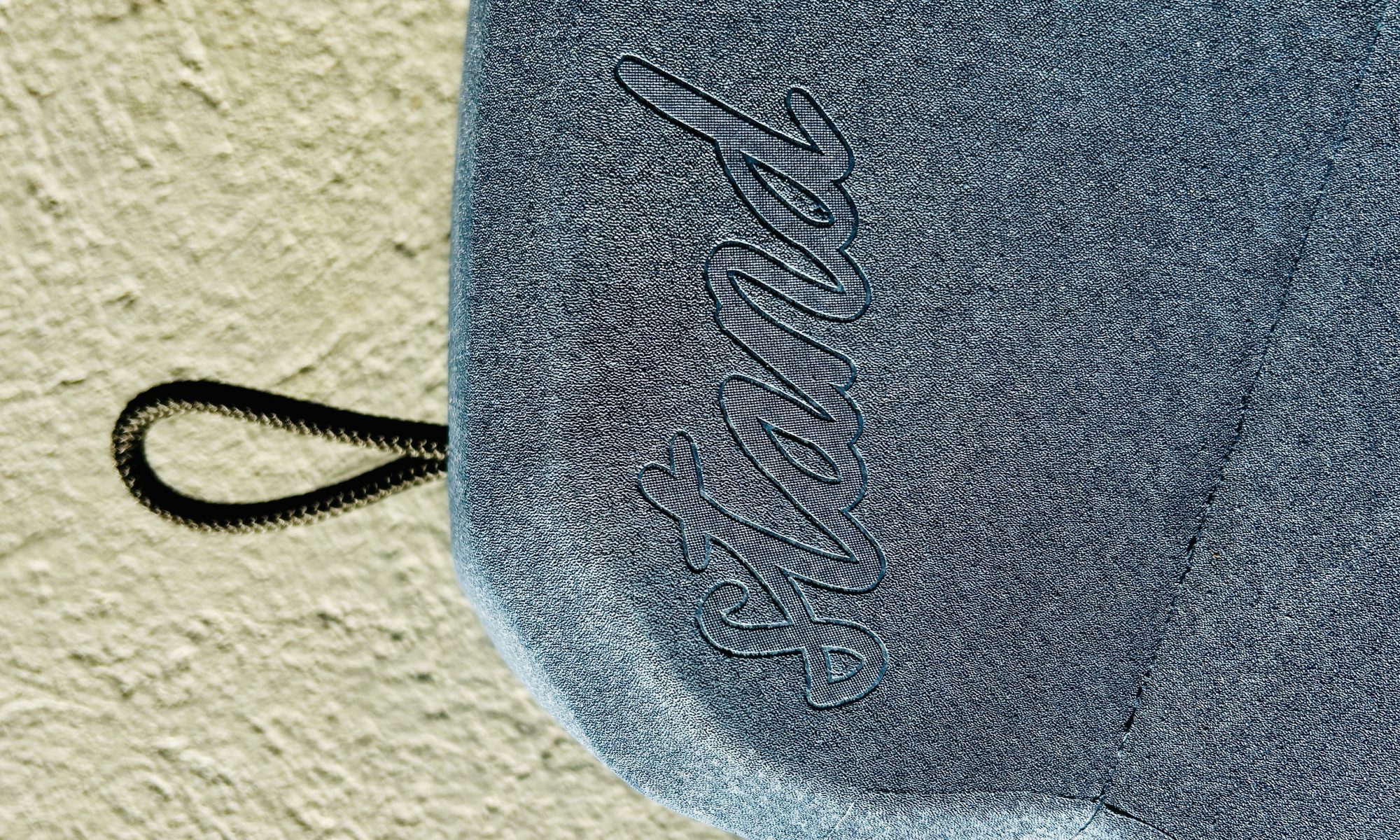 Nahaufnahme eines blauen, strukturierten Materials mit dem eingeprägten Schriftzug „Stand“ in Schreibschrift und einer schwarzen Kordelschlaufe.