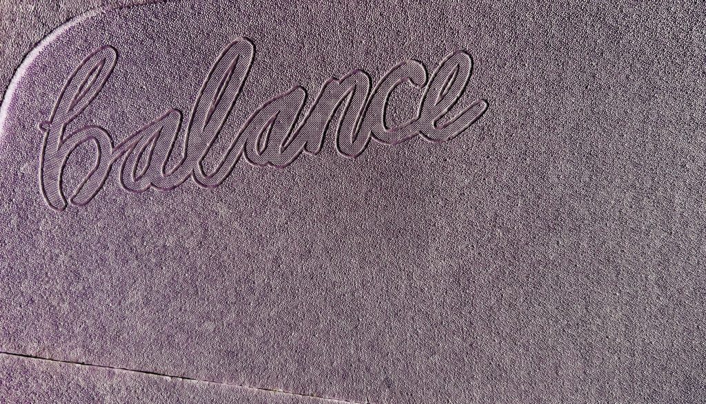 Nahaufnahme der strukturierten Oberfläche eines hellvioletten hockblocs mit dem eingeprägten Wort „Balance“ in eleganter Schreibschrift.