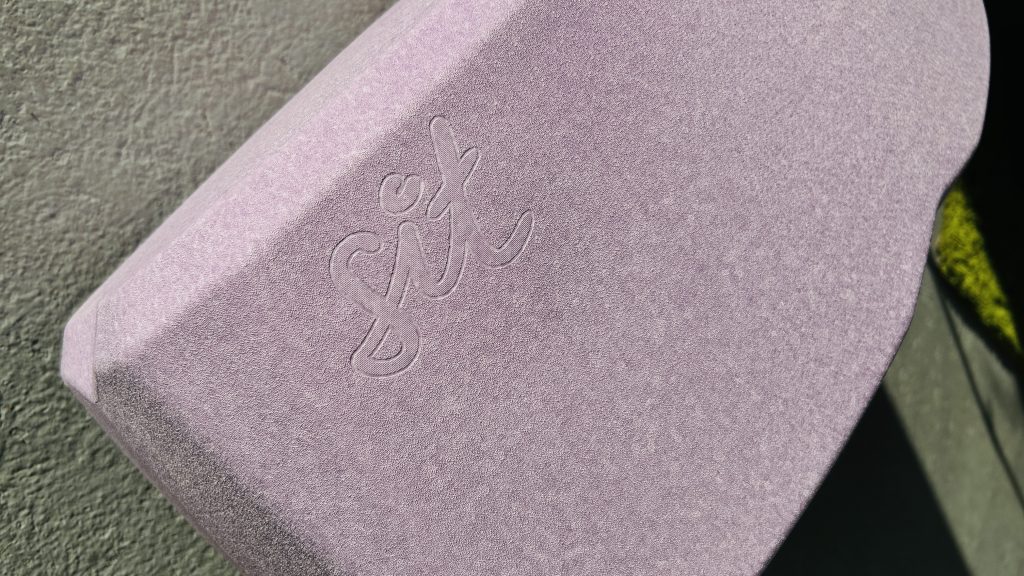 Nahaufnahme eines hellvioletten, strukturierten Blocks mit dem eingeprägten Wort „sit“ in geschwungener Schreibschrift.