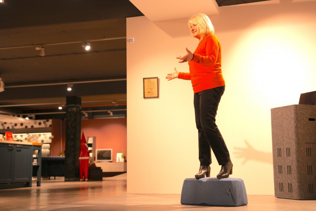 Eine Frau steht mit beiden Beinen auf einem blauen Sitzkissen, um dessen Belastbarkeit und Stabilität als Tritthilfe zu demonstrieren.