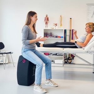 Physiotherpeutin behandlet Patientin und sitzt auf dem hockbloc